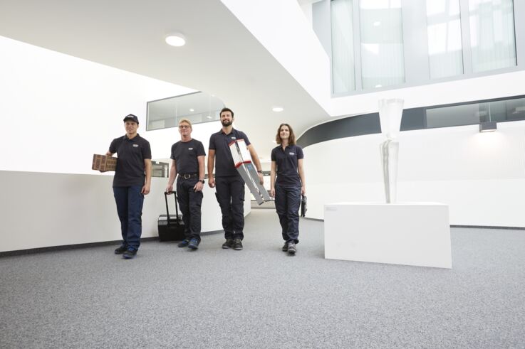 Four GEZE service technicians walk down a corridor in a modern building with their work materials.