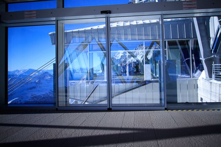 Automatic sliding door with panoramic view of snow-covered mountain landscape at a mountain station.