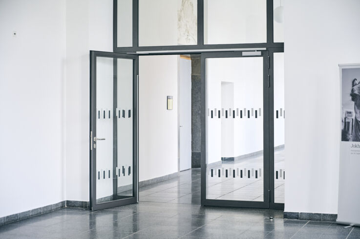 Open glass door with black metal frame in a bright corridor.